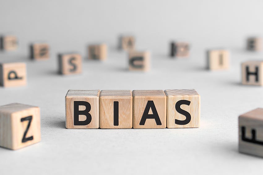Holzwürfel mit schwarzen Buchstaben darauf bilden das Wort "BIAS" vor einem unscharfen Hintergrund mit weiteren einzelnen Buchstabenwürfeln.